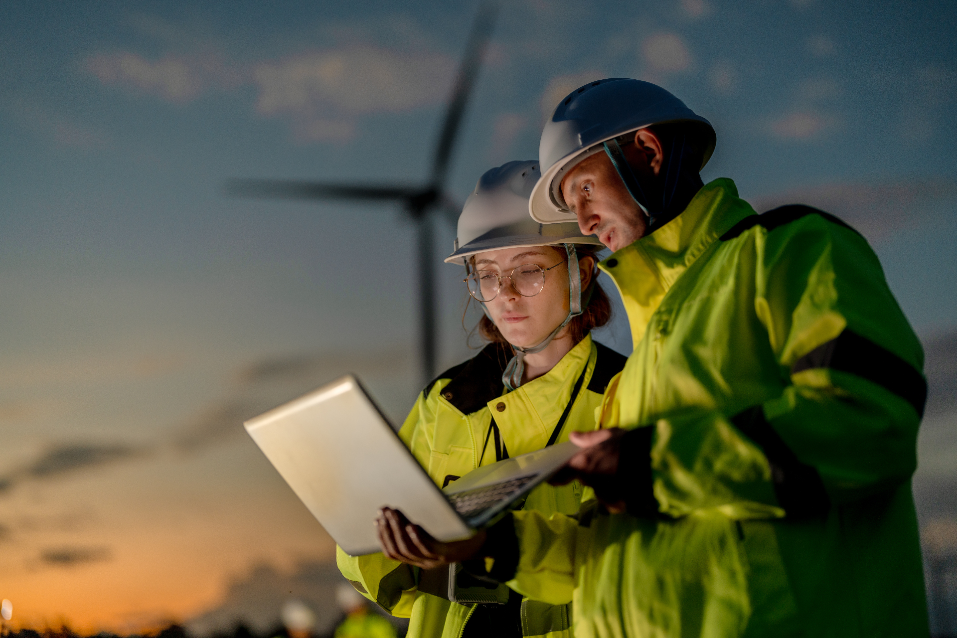 Tecnici al lavoro davanti a una turbina eolica al tramonto